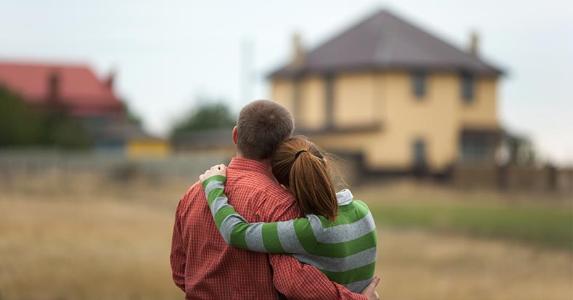 young-couple-hugging-eachother-looking-at-house-distance_573x300.jpg