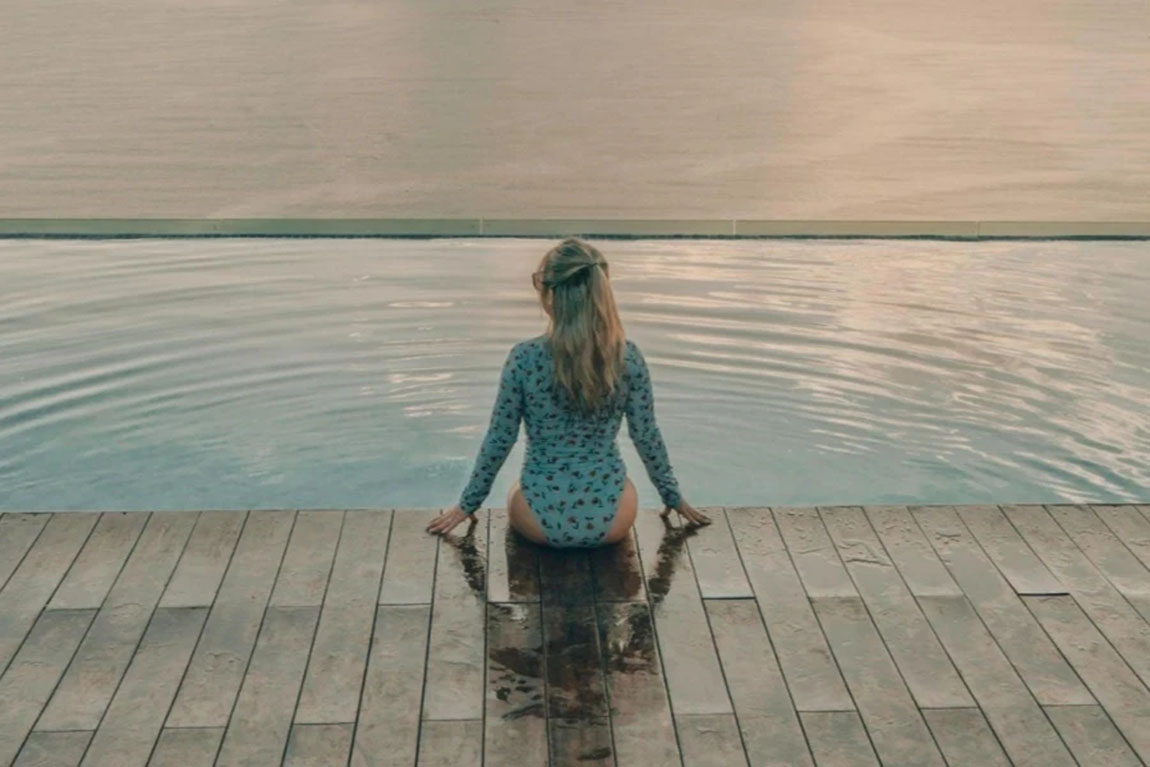 A-Woman-in-Bathing-Suit-Sitting-on-the-Poolside.webp.jpg