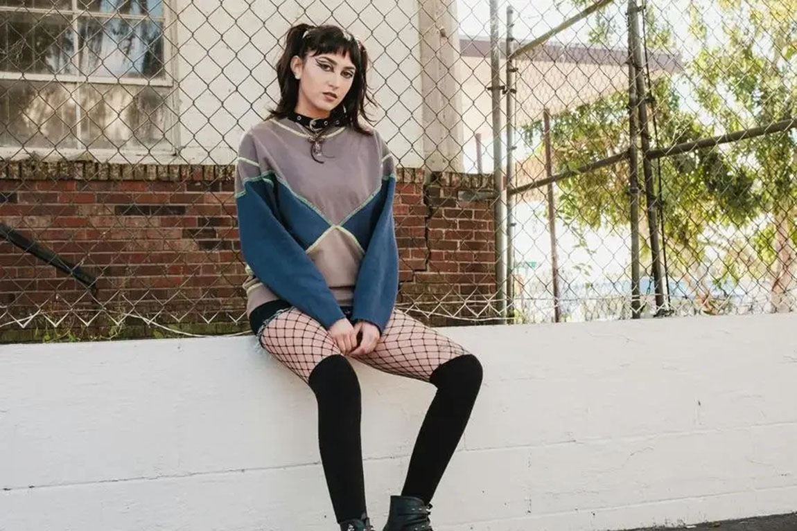Woman-in-Sweatshirt-and-Fishnet-Stocking-Sits-on-Wall-by-Airam-Dato-on.webp.jpg