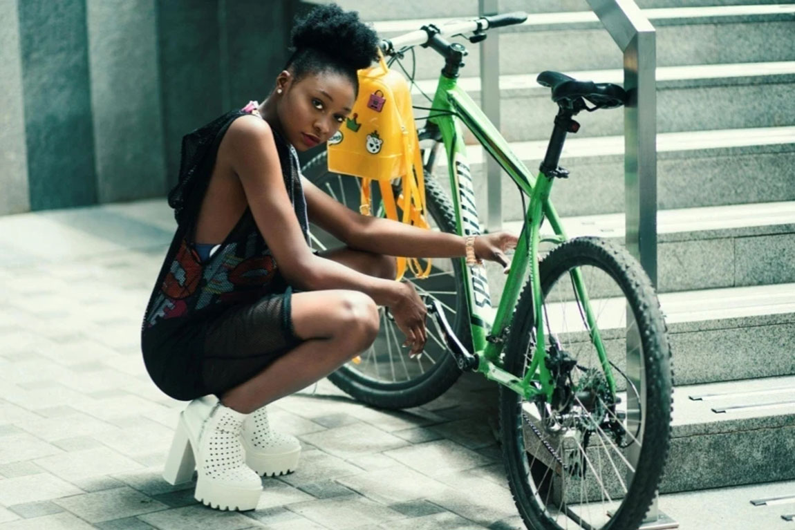 Woman-wearing-black-dress-squatting-next-to-green-bicycle.webp.jpg
