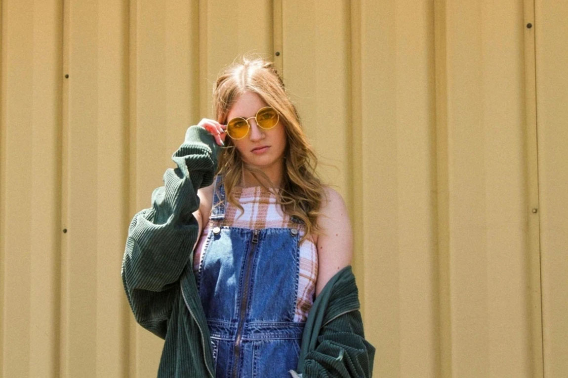 Photo-of-Woman-in-Blue-Denim-Dungaree-Green-Corduroy-Jacket-and-Yellow-Sunglasses-Posing.webp.jpg