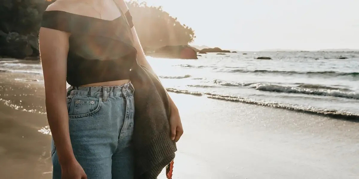 Person-Stands-On-Sandy-Beach-Looking-Out-To-The-Water.webp.jpg