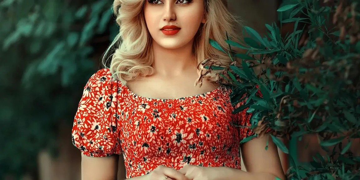 A-stylish-woman-in-a-red-floral-dress-standing-amidst-lush-green-foliage-by-zana-pq.webp.jpg