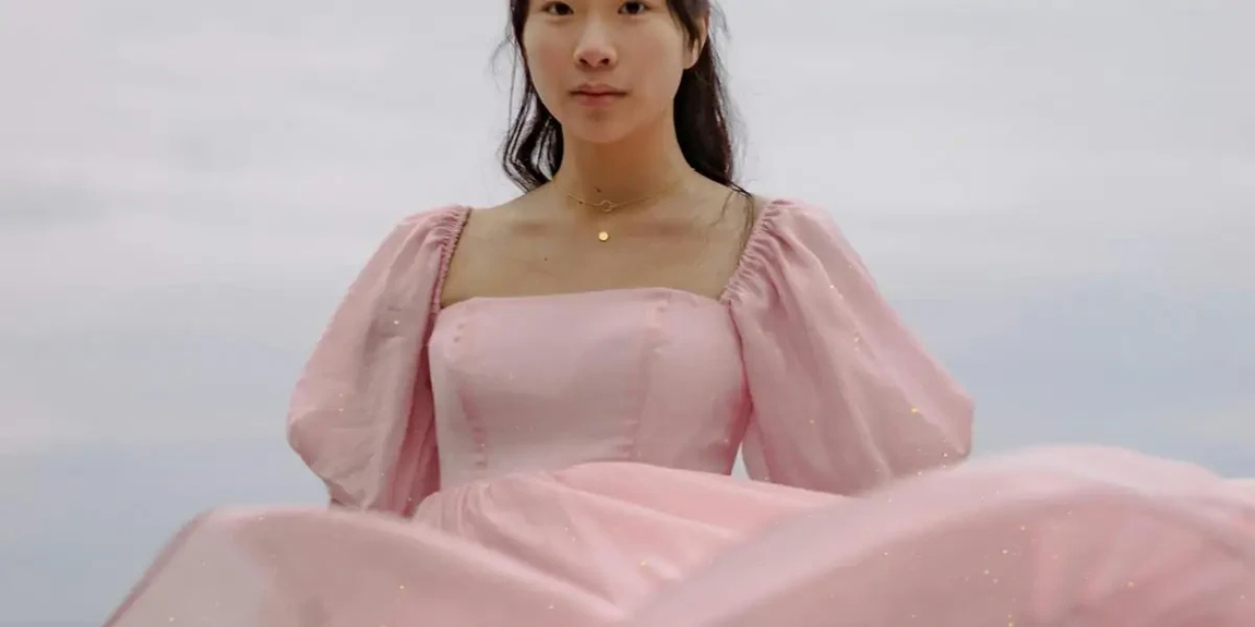 A-woman-in-a-pink-puff-sleeve-dress-stands-against-a-serene-seascape-backdrop-by-jasmin-chew.webp.jpg