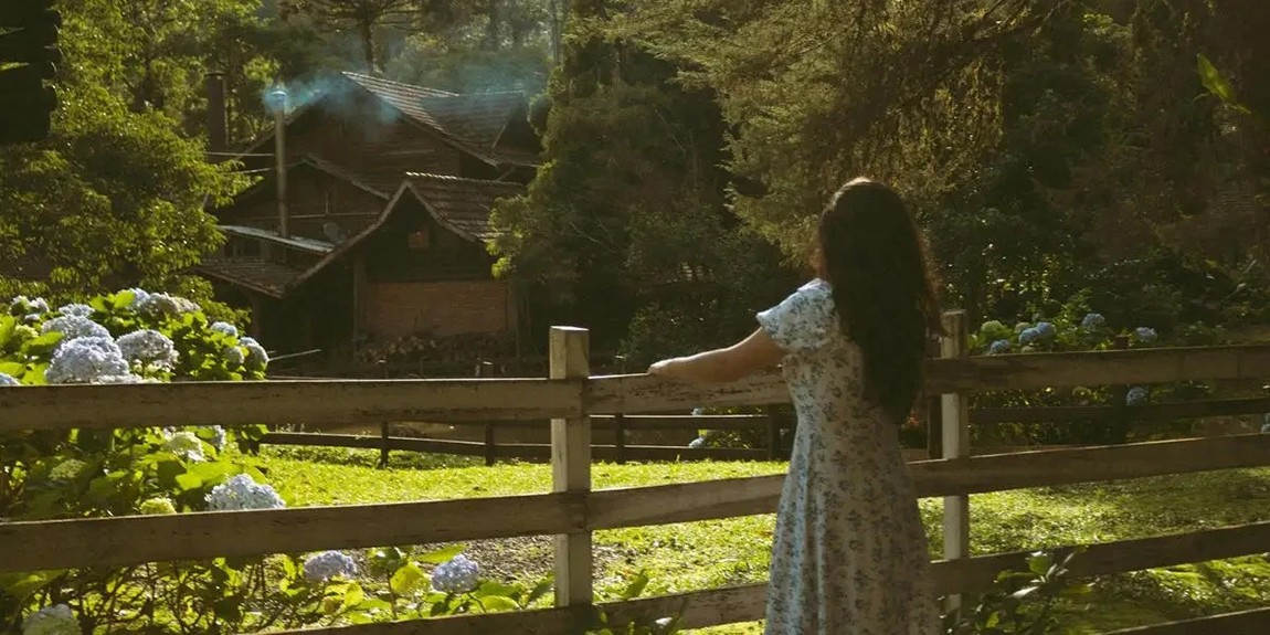Woman-in-a-floral-dress-views-a-serene-countryside-house-from-a-wooden-fence-by-Bruna-Fossile.webp.jpg