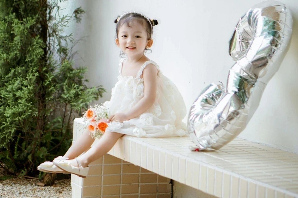 Girl-in-White-Dress-Sitting-with-Birthday-Balloon-on-Bench.webp.jpg