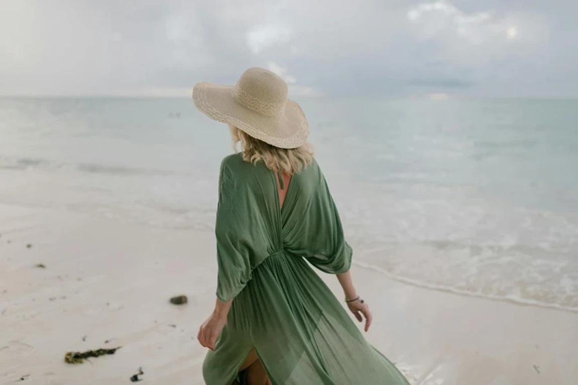 Back-view-of-unrecognizable-female-tourist-wearing-straw-hat-and-summer-dress-standing-on-seashore-in-cloudy-day.webp.jpg