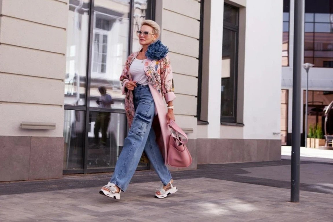 Stylish-mature-woman-walks-near-city-building-wearing-cargo-jeans-pink-floral-trench-coat-sunglasses-and-handbag.webp.jpg