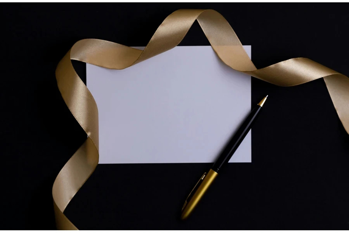 A-gold-pen-a-white-piece-of-paper-and-a-gold-ribbon-lie-on-a-white-background.webp.jpg