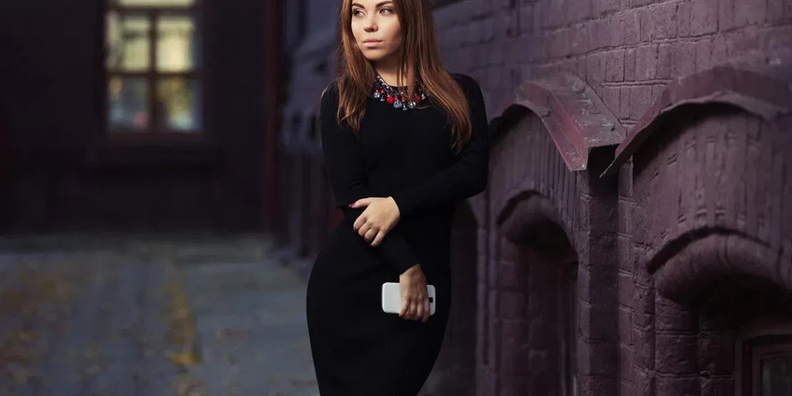 Young-woman-with-a-cell-phone-walking-on-city-street-Stylish-fashion-model-with-long-straight-hair-in-black-sweater-dress.webp.jpg