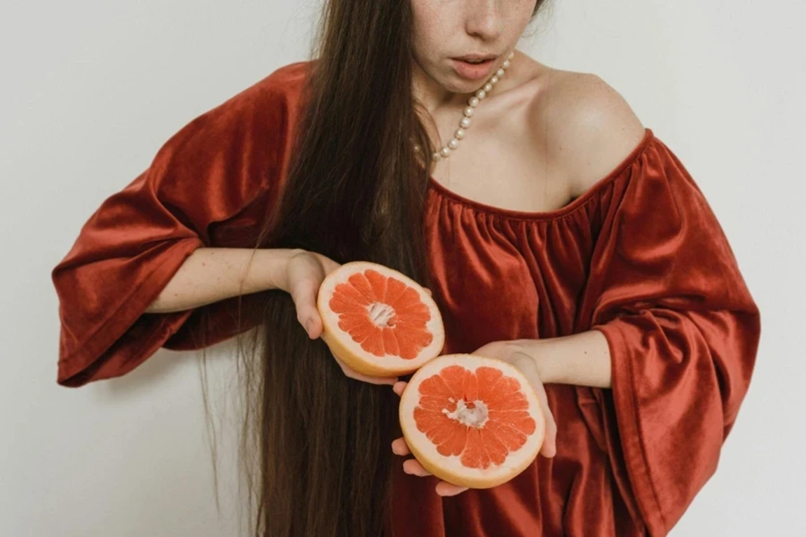 Woman-in-a-red-dress-and-pearl-necklace-holding-a-sliced-grapefruit.webp.jpg